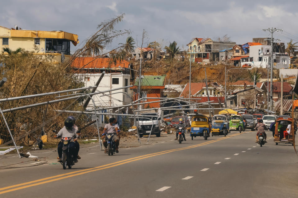 In this photo provided by Greenpeace, residents move by toppled posts due to Typhoon Rai in Surigao City, southern Philippines Monday Dec. 20, 2021. The governor of a central Philippine province devastated by Typhoon Rai last week pleaded on radio Tuesday for the government to quickly send food and other aid, warning that without outside help, army troops and police forces would have to be deployed to prevent looting amid growing hunger. (Jilson Tiu/Greenpeace via AP)