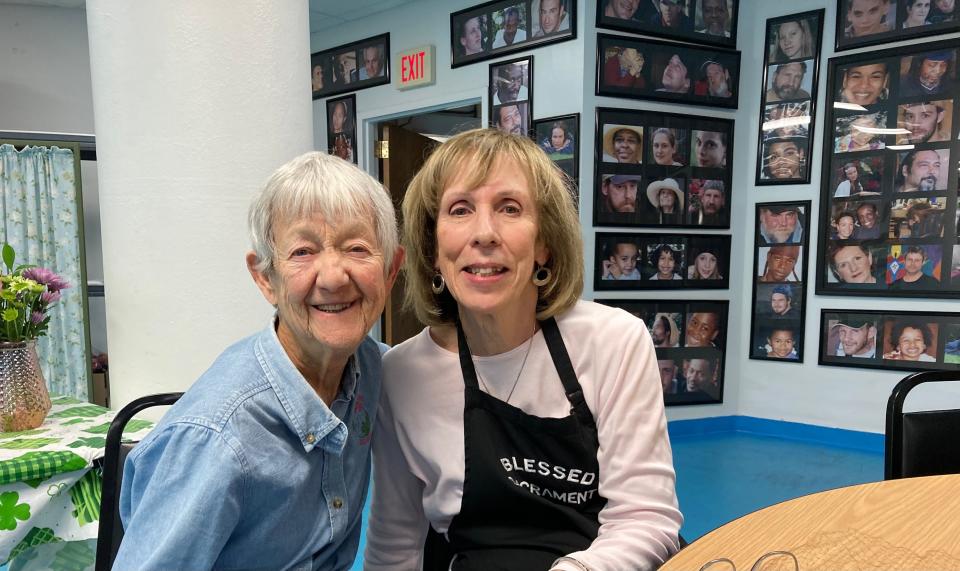 Volunteer Terry Smith and director Mary Jo Lightholder sit in the room dedicated to the Blessed Sacrament Supper Program. Behind them is a wall of photographs of guests that were taken by the late Kathleen Nichols, a volunteer cook and baker.