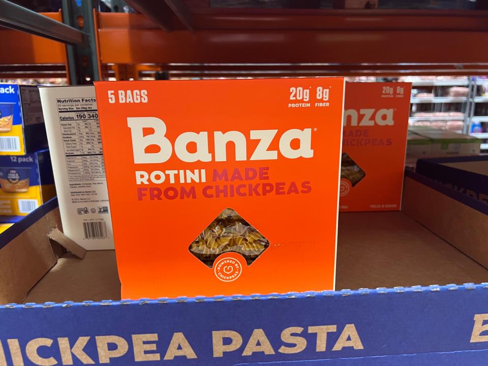 An orange box of Banza rotini with a window into the box showing pasta on shelf at Costco