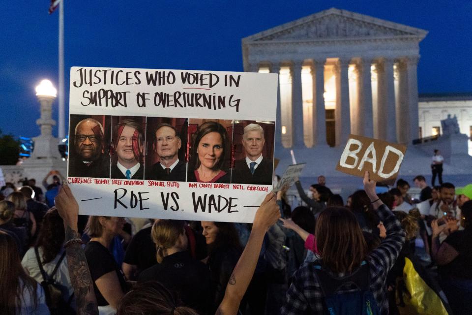 Nikki Tran of Washington, holds up a sign with pictures of Supreme Court Justices Clarence Thomas, Brett Kavanaugh, Samuel Alito, Amy Coney Barrett, and Neil Gorsuch, as demonstrators protest outside of the U.S. Supreme Court, Tuesday, May 3, 2022, in Washington.