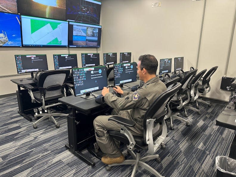 Brig. Gen. Jeffery T. Geraghty sitting at a video game wheel and pedal set that will be used to control unmanned ground vehicles on the Eglin Range.