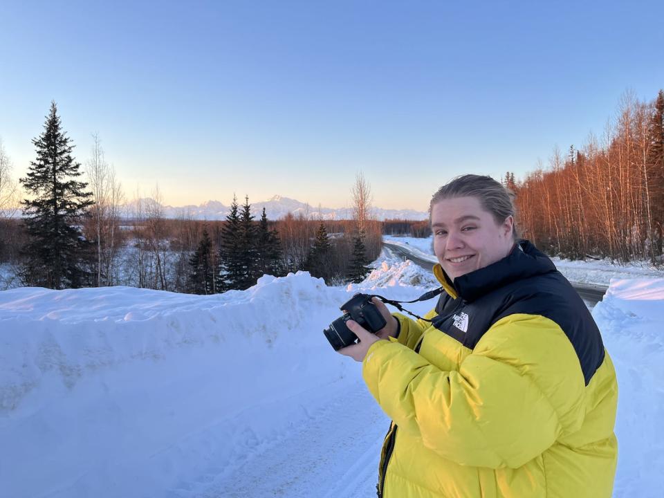 Abby's travel companion in yellow jacket holding camera in snowy Alaskan wilderness