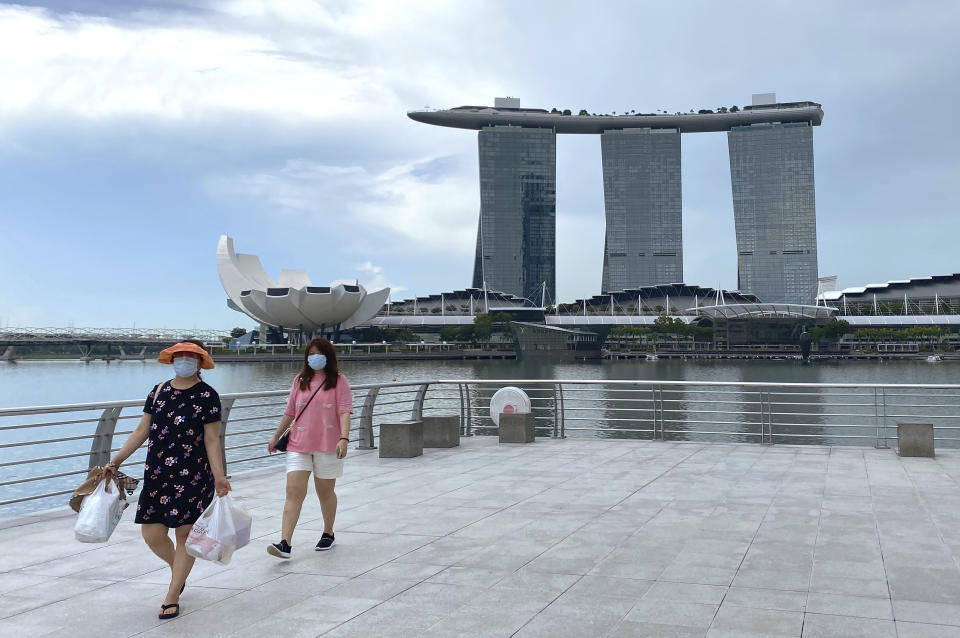 Visitors wear masks while walking around Merlion Park, a popular tourist destination, with the Marina Bay Sands in the background in Singapore Monday, May 31, 2021. Singapore's Prime Minister Lee Hsien Loong said Monday that controls to lower coronavirus infections were working, while announcing a move to vaccinate students after a spate of transmissions in schools and learning centers. (AP Photo/Annabelle Liang)