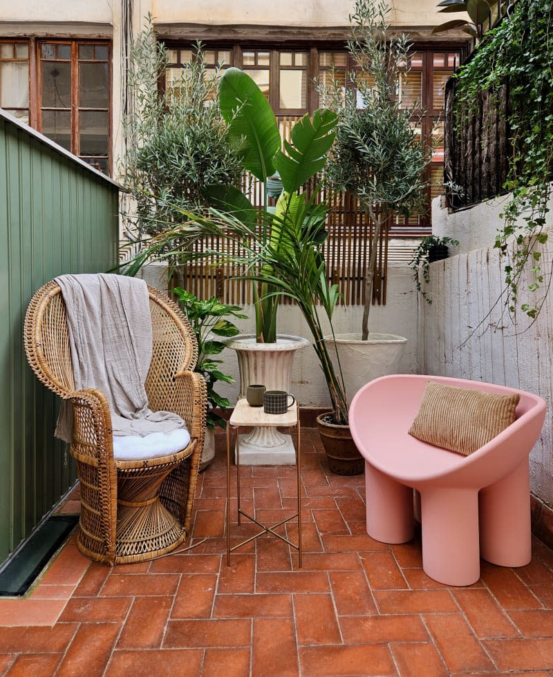 Chairs sit outside near a coffee table surrounded by plants.