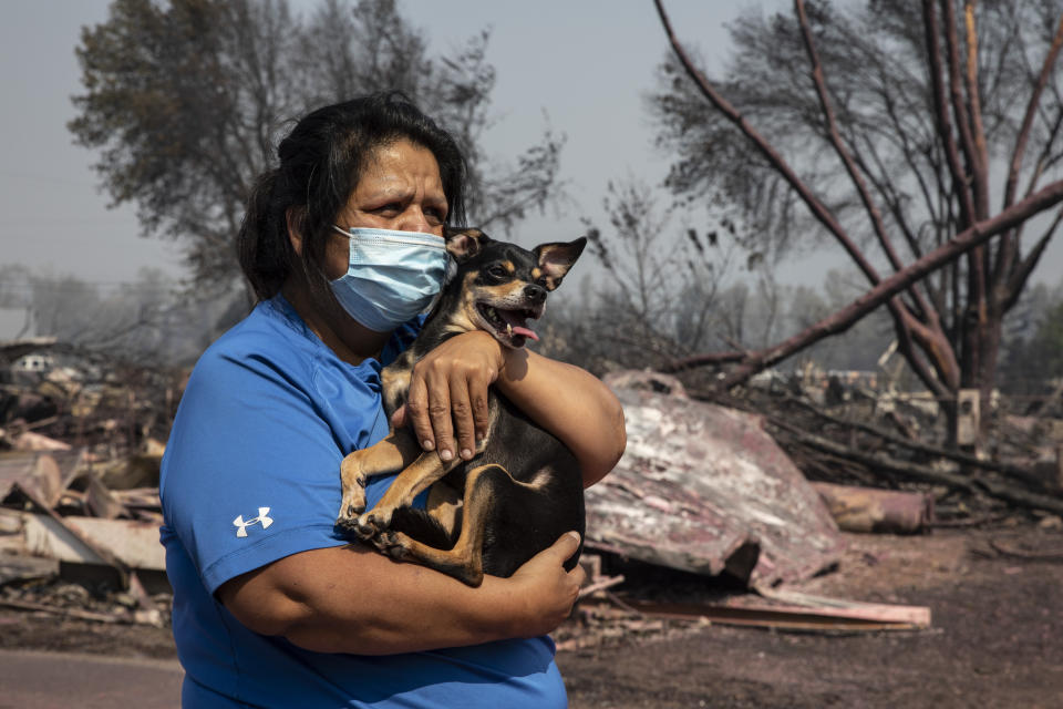 Dora Negrete holds her dog Scoovy, standing by her destroyed mobile home at the Talent Mobile Estates as wildfires devastate the region on Thursday, Sept. 10, 2020 in Talent, Ore. (AP Photo/Paula Bronstein)