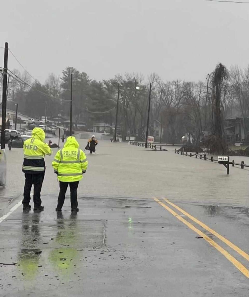 An employee with the Hendersonville Fire Department, left, and Hendersonville Police Department watch as a member of the Henderson County Rescue Squad goes to help someone in need of evacuation from a building that had flooded on Jan. 9 on Grove Street.