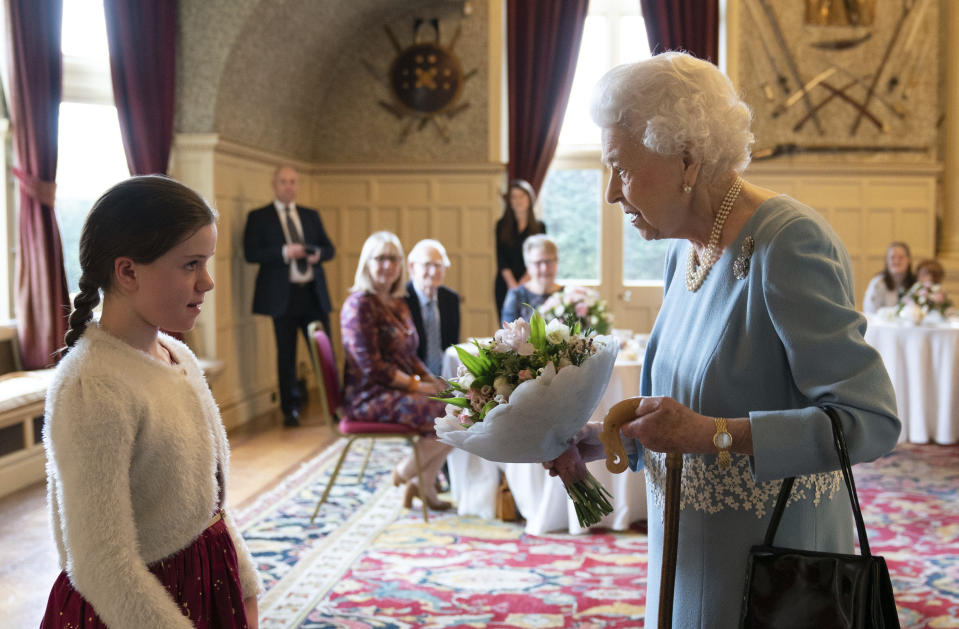 FILE - Britain's Queen Elizabeth II receives a posy from Harriet Reeve, 9, during a reception to celebrate the start of the Platinum Jubilee, at Sandringham House, her Norfolk residence, in Sandringham, England, Saturday, Feb. 5, 2022. Britain is getting ready for a party featuring mounted troops, solemn prayers — and a pack of dancing mechanical corgis. The nation will celebrate Queen Elizabeth II’s 70 years on the throne this week with four days of pomp and pageantry in central London. (Joe Giddens/Pool Photo via AP, File)