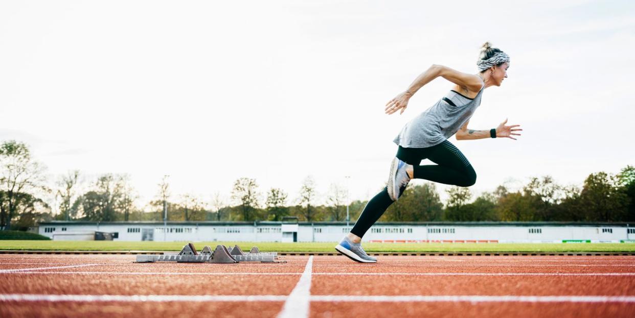 a woman wearing sports clothing sprinting off the starting blocks on an outdoor running track