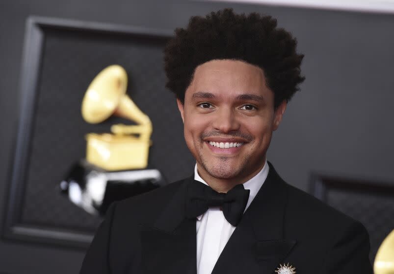 A man smiling in a black tuxedo and bowtie against a Grammys backdrop