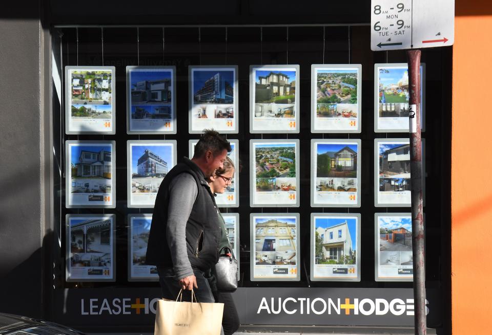 A couple walks past a real estate agent's window advertising houses for sale. (Credit: William West, AFP via Getty Images)