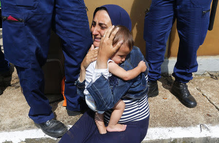 Hungarian policemen stand by a migrant holding a baby at the railway station in the town of Bicske, Hungary, September 3, 2015. REUTERS/Laszlo Balogh