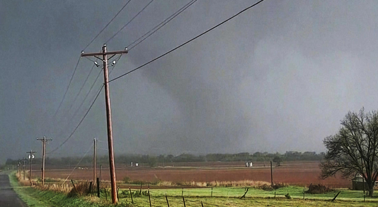 In this image taken from video, a massive funnel-shaped storm cloud makes its way over a road, as seen from a car, in Cole, Okla., Wednesday night, April 19, 2023. (KOCO-TV via AP)