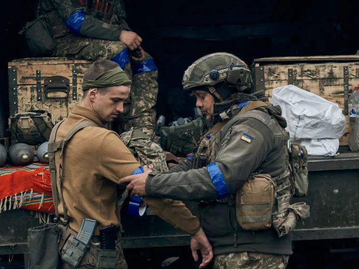 A Ukrainian soldier helps another adjust a blue identification ribbon on his sleeve in the recently retaken Kupiansk in the Kharkiv region of Ukraine on Sept. 14, 2022.
