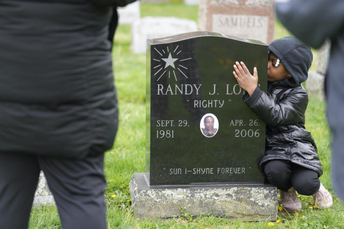 Xia'la Long kisses her uncle Randy Long's tombstone while posing for a picture for her mother, Tamara Long, and grandmother, Debra Long, in Poughkeepsie, N.Y., April 19, 2023. An AP examination of data from 23 states shows that Black people are disproportionately denied aid from programs that reimburse victims of violent crime. (AP Photo/Seth Wenig)