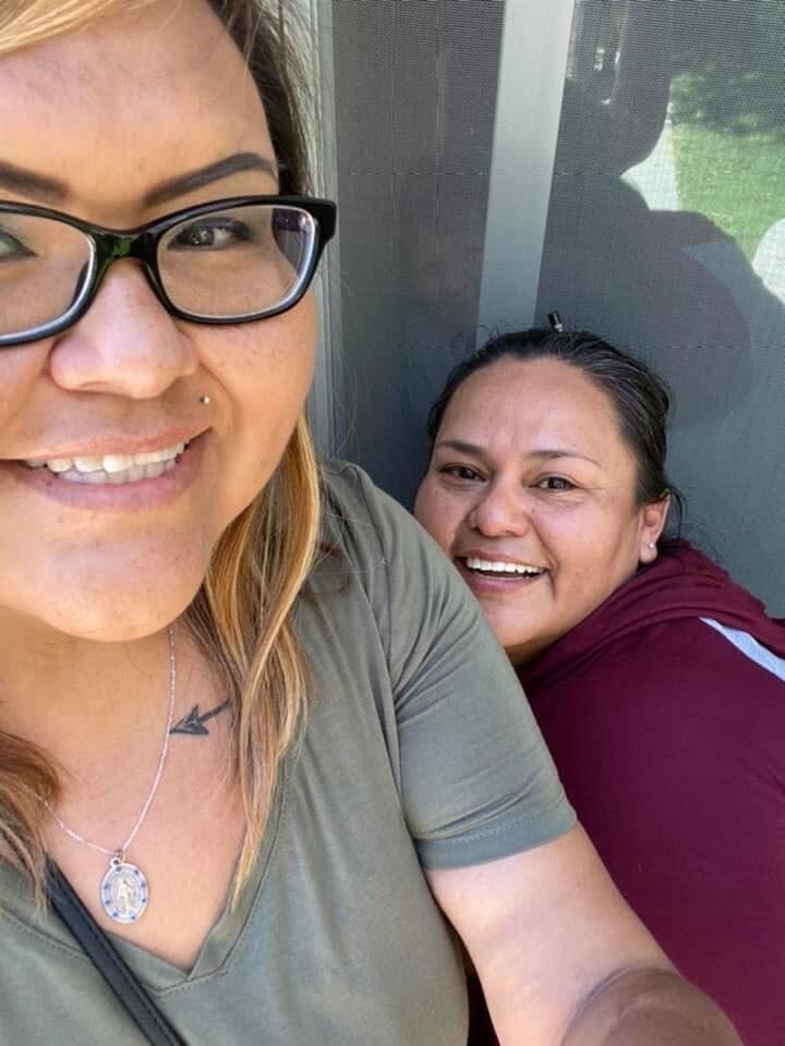 In this April 28, 2020 photo provided by Shannon Todecheene , Todecheene, left, and her sister Erin Gonzales, right, visit their mother Carol Todecheene, background, through a window at a rehabilitation center in Tucson, Ariz. Carol Todecheene was among those severely hit with the coronavirus. (Shannon Todecheene via AP)