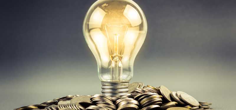 A lit light bulb sits in a pile of coins.