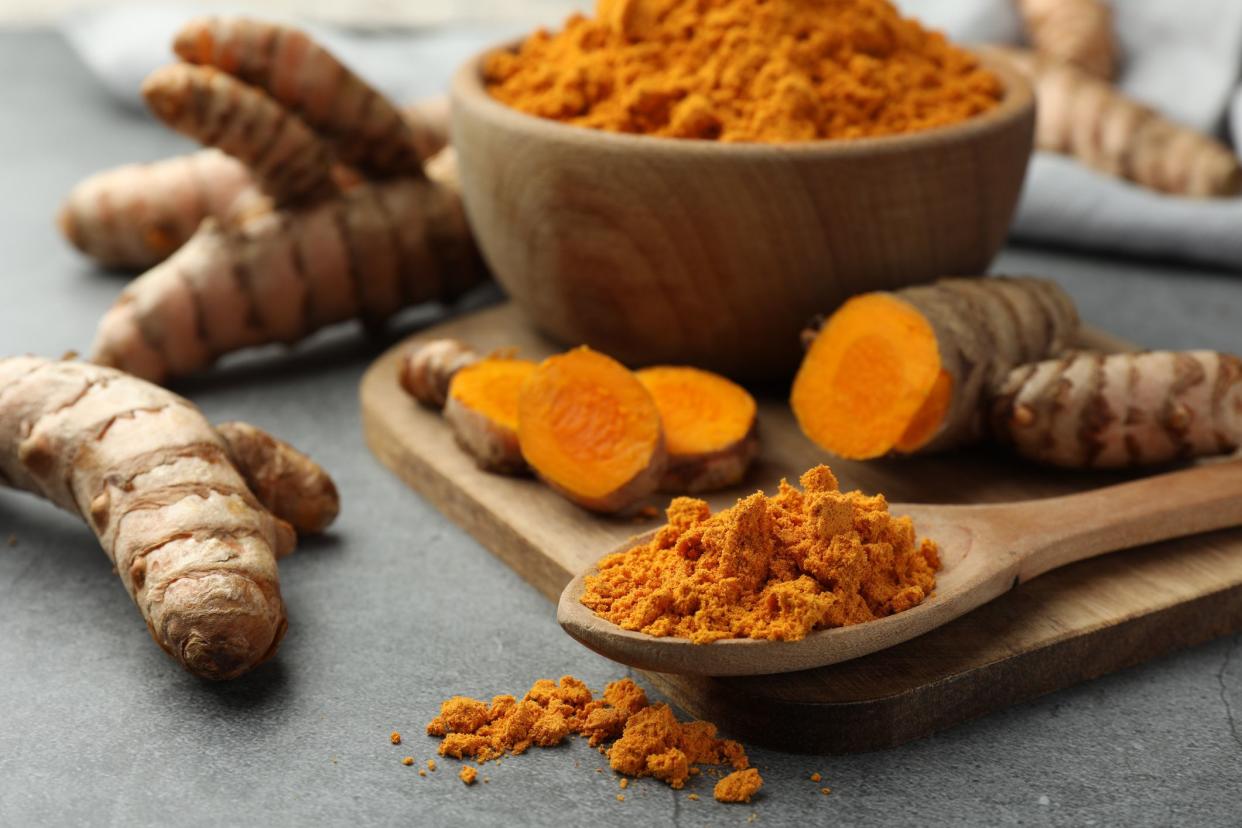 Aromatic turmeric powder and raw roots on grey table, closeup