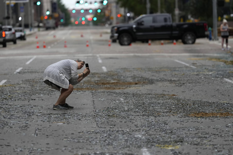 Cheryl Herpich takes a photograph of a downtown building with blown out windows in the aftermath of a severe thunderstorm Friday, May 17, 2024, in Houston. Thunderstorms pummeled southeastern Texas on Thursday killing at least four people, blowing out windows in high-rise buildings and knocking out power to more than 900,000 homes and businesses in the Houston area. (AP Photo/David J. Phillip)