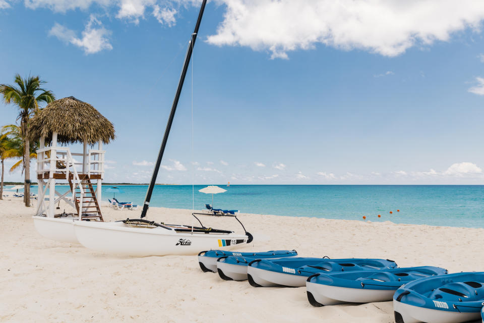 A row of kayaks and a catamaran lined up on the beach of a Sunwing resort in Cayo Largo, Cuba
