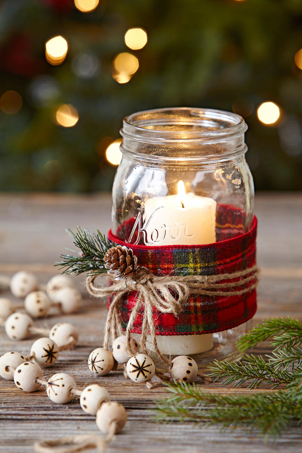 This image shows a pillar candle in a glass jar, decorated for the holiday season. (Jason Donnelly/Better Homes & Gardens via AP)