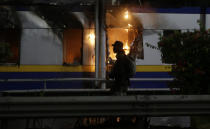 A man walk neat toll gate burn in the background during a protest outside the parliament in Jakarta, Indonesia Tuesday, Sept. 24, 2019. Police fired tear gas and water cannons Tuesday to disperse thousands of rock-throwing students protesting a new law that they said has crippled Indonesia's anti-corruption agency.(AP Photo/Achmad Ibrahim)