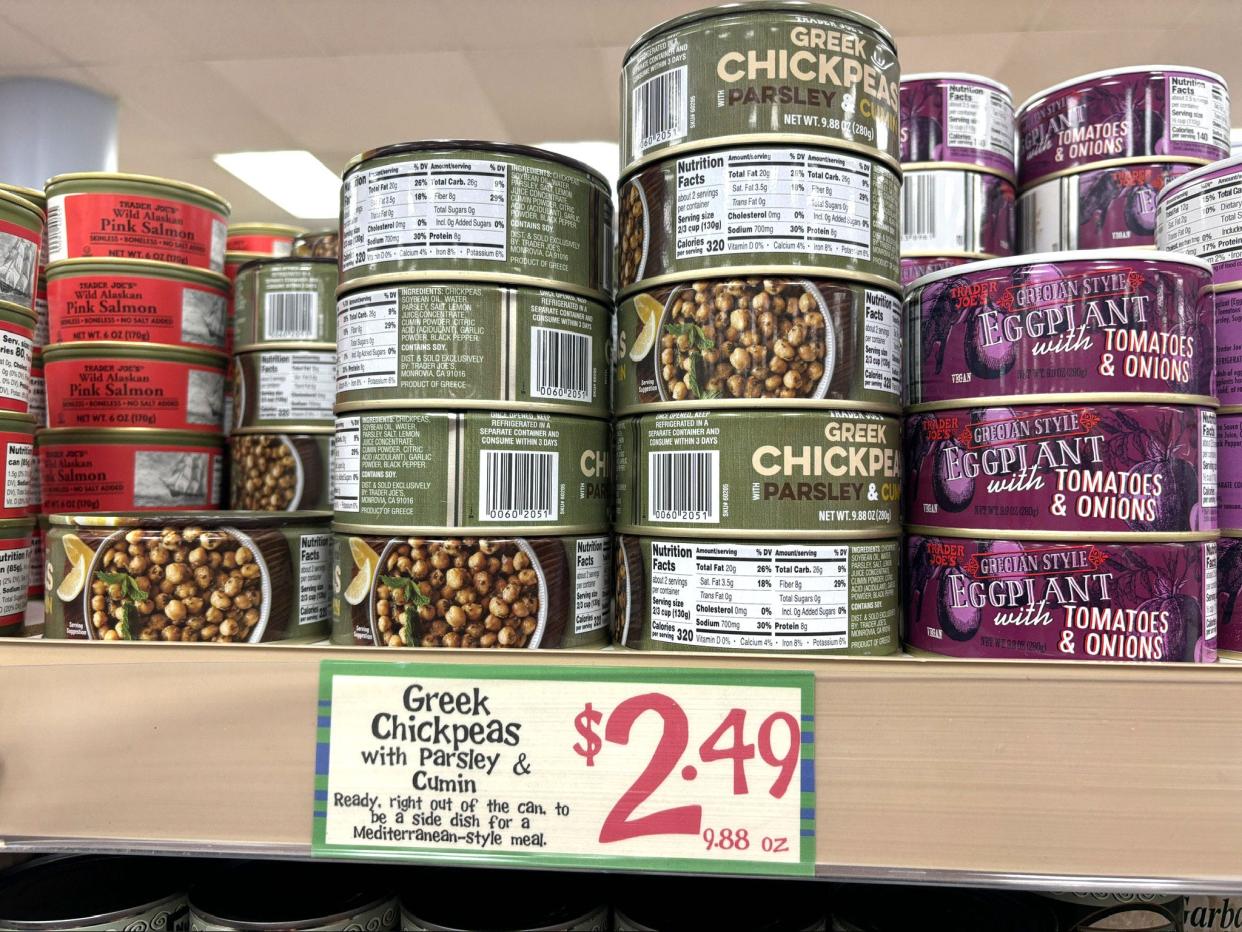 Cans of Greek chickpeas with Parsley and cumin on a shelf at Trader Joe's. The price tag below the cans reads $2.49.