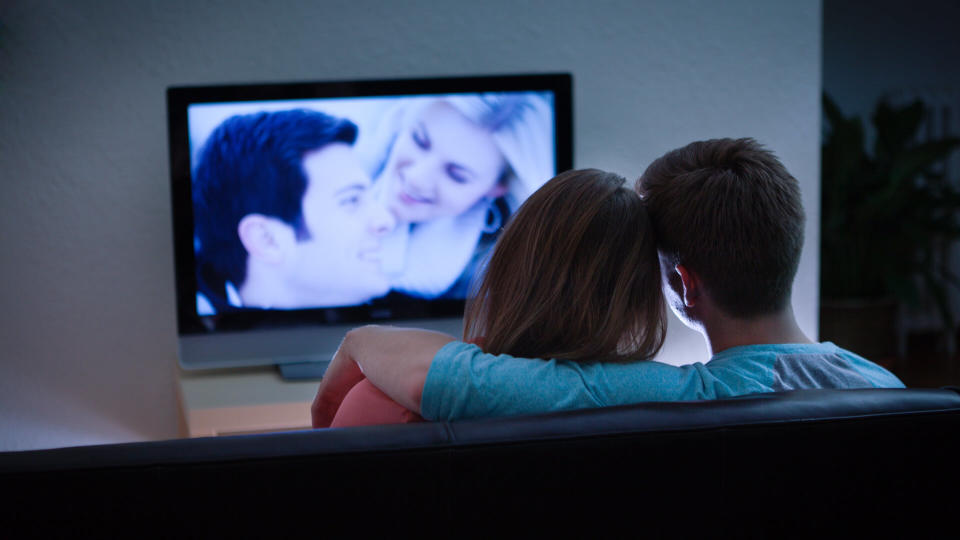 A young Caucasian couple at home watching a romantic program show on TV together in the evening.