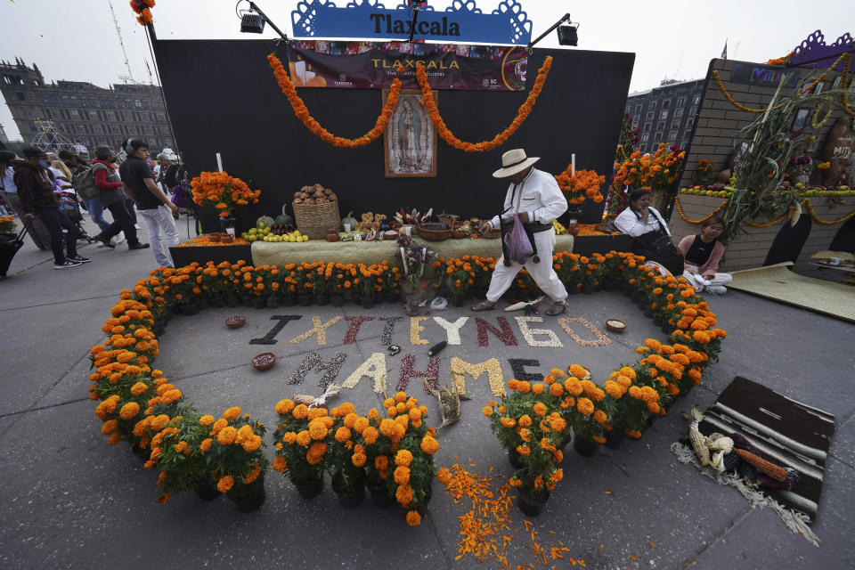 Un hombre adorna un altar con flores de cempasúchil en la plaza principal de la Ciudad de México, el Zócalo, como parte de las festividades del Día de los Muertos en la Ciudad de México, el viernes 28 de octubre de 2022. Durante las celebraciones del Día de los Muertos, los vivos recuerdan y honran a sus queridos difuntos, pero con celebración, no con tristeza. (AP Foto/Marco Ugarte)