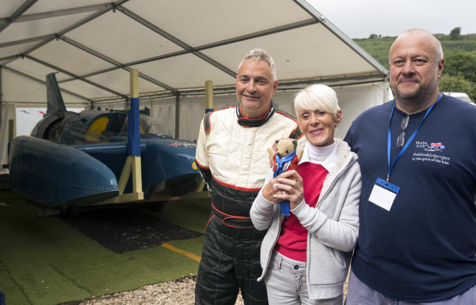 Hydroplane Pilot Ted Walsh, left, Gina Campbell the daughter of pilot Donald Campbell and engineer Bill Smith pose for a photo with the restored Bluebird K7 before it takes to the water for the first time in more than 50 years off the Isle of Bute on the west coast of Scotland, Saturday Aug. 4, 2018. The famed jet boat Bluebird has returned to the water for the first time since a 1967 crash that killed pilot Donald Campbell during a world speed-record attempt. Watched by Campbell's daughter Gina Campbell, the restored Bluebird was lowered Saturday into Loch Fad on Scotland's Isle of Bute, where it will undergo low-speed tests.(David Cheskin/PA via AP)