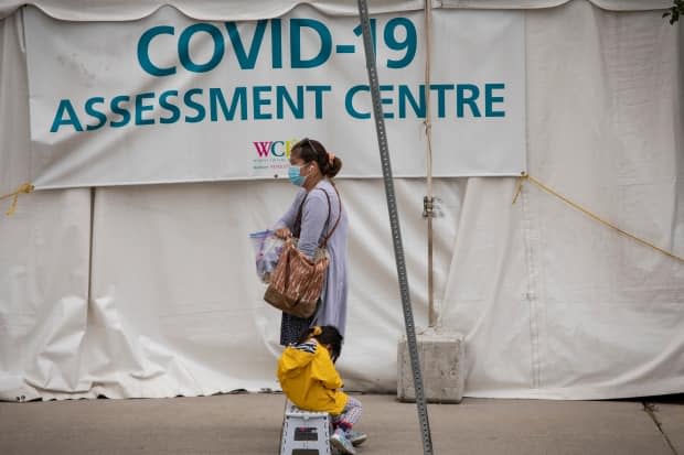 A woman walks by a COVID-19 assessment centre. Experts say rapid tests are urgently needed in essential workplaces and schools, which largely remain open under Ontario's new emergency brake shutdown. (Evan Mitsui/CBC - image credit)