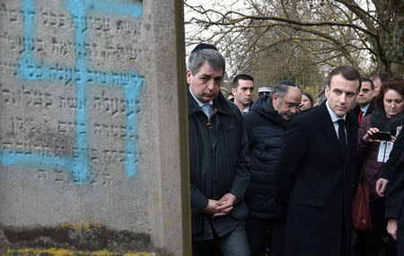 French President Emmanuel Macron looks at a grave vandalised with a swastika during a visit at the Jewish cemetery in Quatzenheim, France February 19, 2019. Frederick Florin/Pool via REUTERS