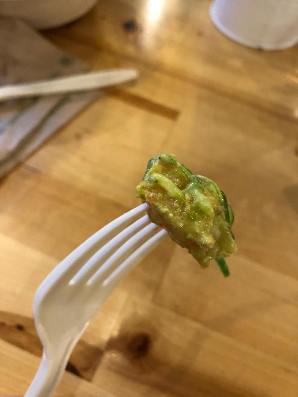 A piece of salmon poke, covered in a pale-green yuzu sauce, on a fork at Poke Papa