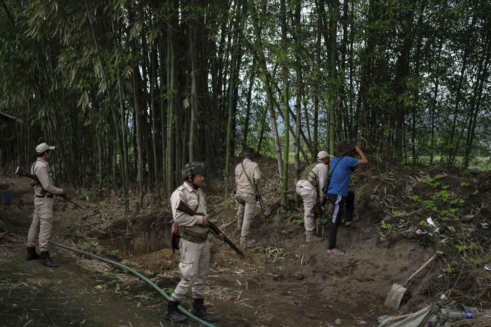 Manipur policemen from Meitei community stand guard as a volunteer, in blue, peers through binoculars monitoring the positions of rival tribal Kuki community bunkers in Kwakta, some 50 kilometers from Imphal, capital of the northeastern Indian state of Manipur, Thursday, June 22, 2023. The state is caught in a deadly conflict between two ethnic communities that have armed themselves and launched brutal attacks against one another. The conflict has also divided state forces, with many defecting to their communities along with their arms and in some cases more sophisticated weaponry like snipers, light machine guns and mortars. (AP Photo/Altaf Qadri)