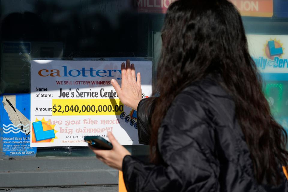 FILE - People touch a window sign for good luck announcing the $2.04 billion-winning Powerball ticket award at Joe's Service Center, a Mobil gas station at Woodbury Road and Fair Oaks Avenue in Altadena, Calif., on Jan. 6, 2023.