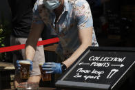 A member of staff wearing a face mask to protect from coronavirus places takeaway pints down on a collection point table for customers to then take, from the entrance of the Althorp pub, which is next to Wandsworth Common in south London, Tuesday, May 26, 2020. As part of the British government coronavirus lockdown pubs are not yet allowed to have customers drinking inside their premises, but are allowed to sell takeaway drinks. (AP Photo/Matt Dunham)