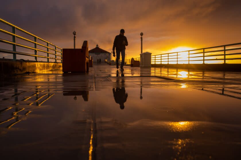 Manhattan Beach, CA - March 21: After a full day of rain, people walk on the Manhattan Beach Pier as the setting sun breaks through clouds, in Manhattan Beach, CA, Tuesday, March 21, 2023. Southern California saw another series of storms Tuesday and Wednesday. (Jay L. Clendenin / Los Angeles Times)