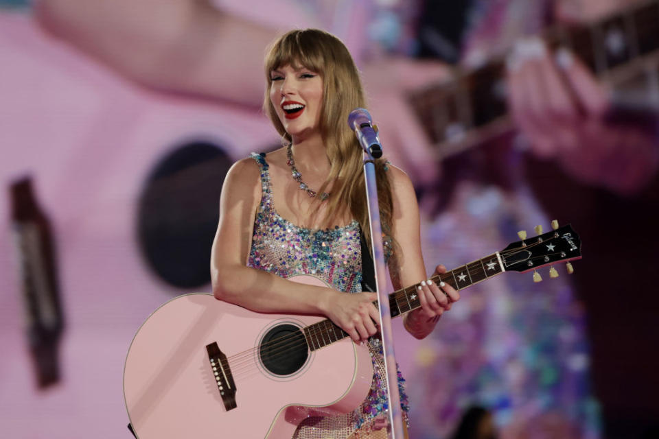 Taylor Swift performs with a guitar, wearing a sparkly bodysuit