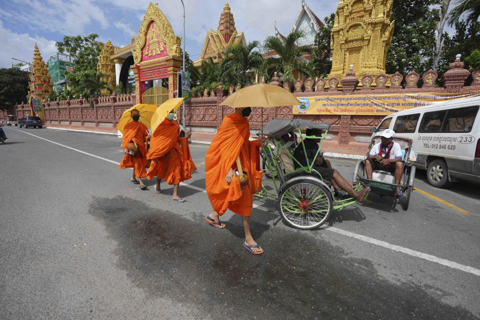 Buddhist monks walk near three-wheeled pedicab drivers who wait for their costumers in Phnom Penh, Cambodia, Friday, June 3, 2022. (AP Photo/Heng Sinith)