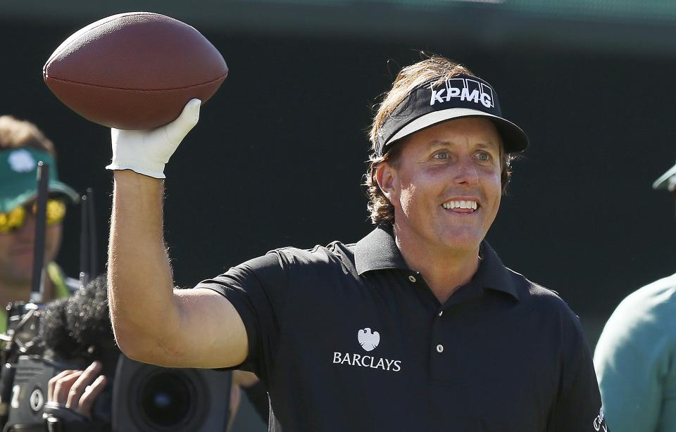 Phil Mickelson smiles as he gets ready to throw a football into the stands at the 16th hole during the third round of the Phoenix Open golf tournament Saturday, Feb. 1, 2014, in Scottsdale, Ariz. (AP Photo/Ross D. Franklin)