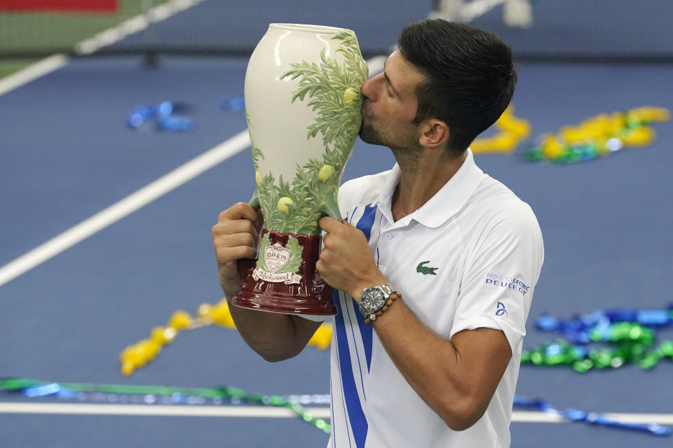 Novak Djokovic, of Serbia, front, kisses his winning trophy after winning his match with Milos Raonic, of Canada, at the Western & Southern Open tennis tournament Saturday, Aug. 29, 2020, in New York. (AP Photo/Frank Franklin II)