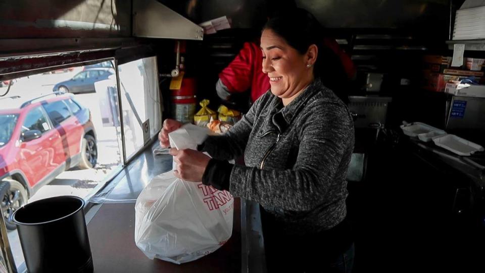 Gabriela Talavera packages an order of birria tacos and consomé while her husband, Fabrizio Sanchez, works at the grill in their La Garnacha de Apapacha food truck.