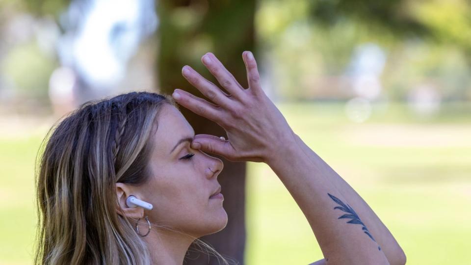 A woman wearing white JBL Tune Flex earbuds doing yoga or Tai chi in a park.