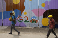 People walk past a construction site covered with G20 summit logo, in New Delhi, India, Thursday, Aug. 24, 2023. As India gears up to host the annual gathering of the Group of 20 industrialized and developing nations, the capital city is undergoing an elaborate makeover. But for many street vendors and shantytowns dotting the city, the beautification of New Delhi has meant displacement and loss of livelihoods. (AP Photo/Manish Swarup)