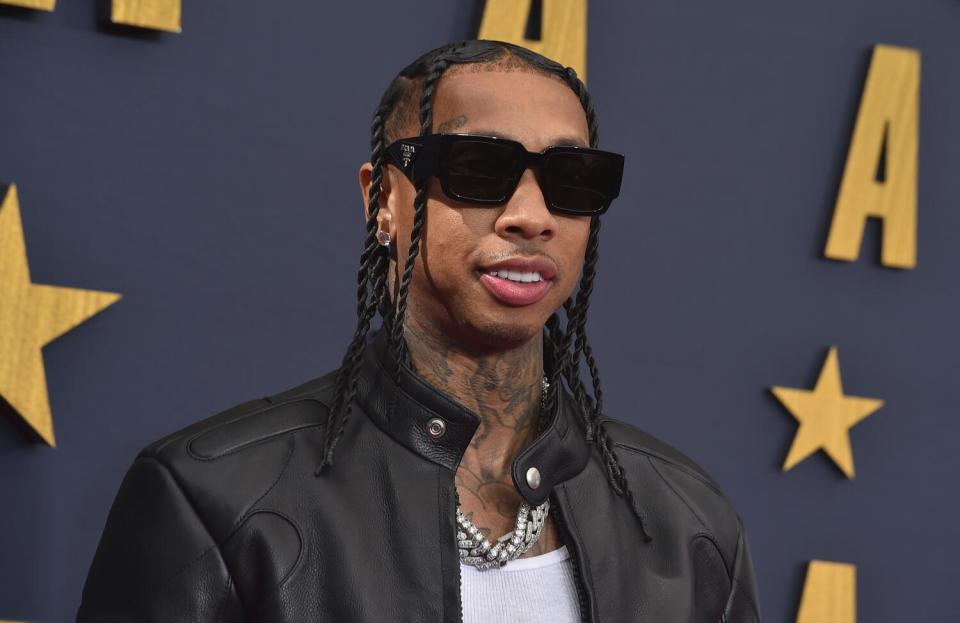 Tyga smiles while wearing dark sunglasses