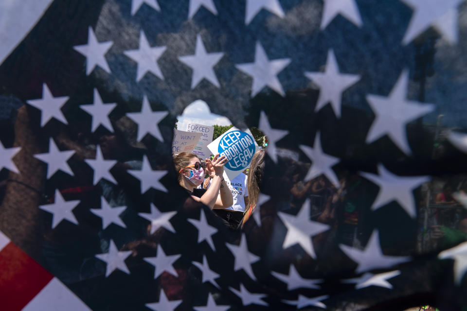 Abortion rights activists are seen through a hole in an American flag as they protest outside the Supreme Court in Washington, Saturday, June 25, 2022. The U.S. Supreme Court's decision to end constitutional protections for abortion has cleared the way for states to impose bans and restrictions on abortion — and will set off a series of legal battles. (AP Photo/Jose Luis Magana)