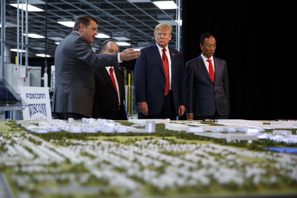 FILE - In this June 28, 2018 photo, President Donald Trump takes a tour of Foxconn with Foxconn chairman Terry Gou, right, and CEO of SoftBank Masayoshi Son in Mt. Pleasant, Wis. Wisconsin Gov. Tony Evers' administration and Foxconn Technology Group say that a massive project planned for the state is moving forward, while disputing Republicans who blamed the new Democratic governor for a change in direction away from manufacturing toward more white collar jobs. Foxconn said Wednesday that it was shifting the focus of the Wisconsin project away from making high-tech flat panel screens for televisions and other products in favor of a research and development hub. (AP Photo/Evan Vucci, File)