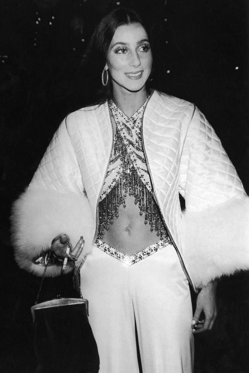 <p>She holds a cigarette while posing in crisscrossed sequined halter top and a fur-trimmed quilted coat.</p>