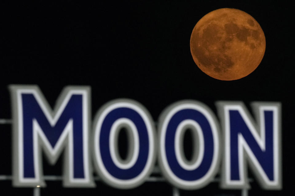 FILE - A supermoon rises beyond a beer sign at Kauffmann Stadium during a baseball game between the Kansas City Royals and the New York Mets, Aug. 1, 2023, in Kansas City, Mo. Stargazers are in for a double treat on Wednesday night, Aug. 30: a rare blue supermoon with Saturn peeking from behind. The cosmic curtain rises Wednesday night with the second full moon of August, the reason it’s considered blue. It’s dubbed a supermoon because it’s closer to Earth than usual, appearing especially big and bright. (AP Photo/Charlie Riedel, File)