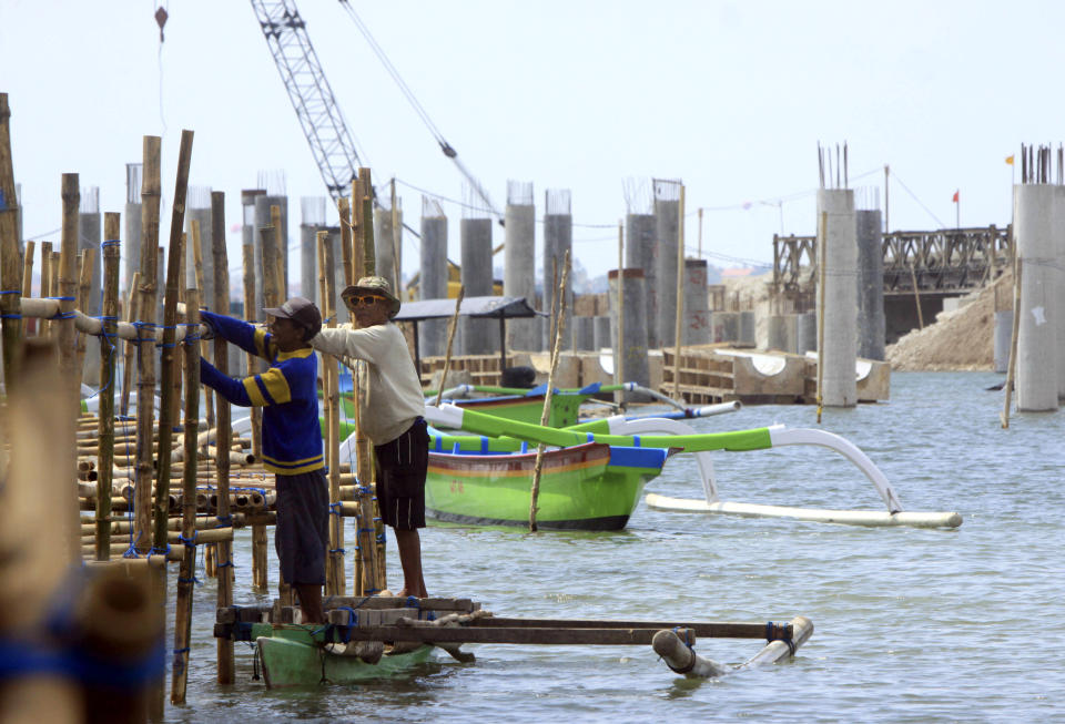 This Aug. 25, 2012 photo shows Balinese men building a bamboo bridge next to a road construction site in Kuta, Bali, Indonesia. It can be hard to find Bali's serenity and beauty amid the villas with infinity pools and ads for Italian restaurants. But the rapidly developing island's simple pleasures still exist, in deserted beaches, simple meals of fried rice and coconut juice, and scenes of rural life. (AP Photo/Firdia Lisnawati)