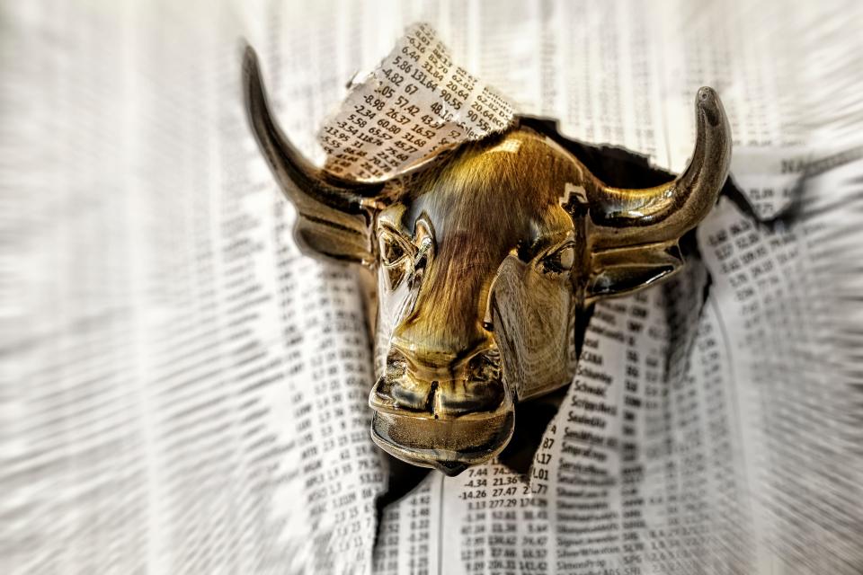 Charging Bull Looking Through Torn Page of Financial Newspaper